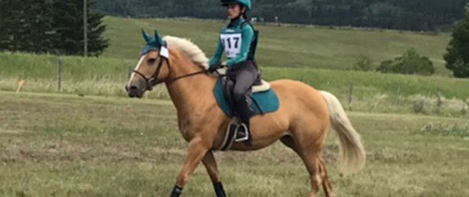 Young rider dressed in green silks riding cross country in a competition on palomino pony