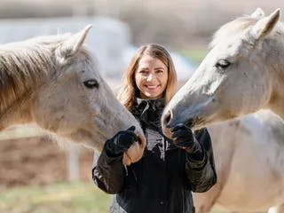 Woman standing with two grey horses nuzzling her