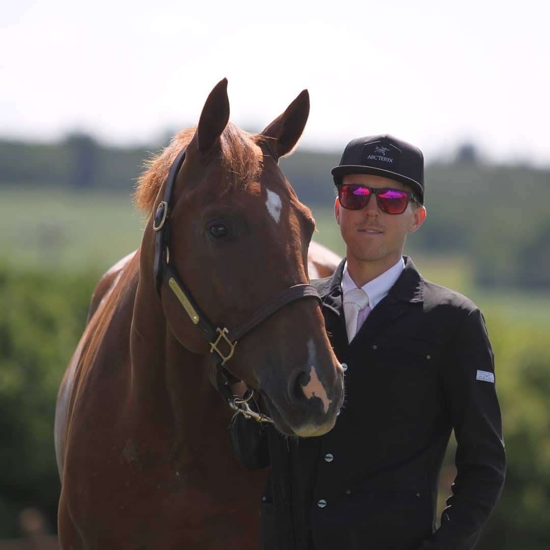 Young man standing next to chestnut horse