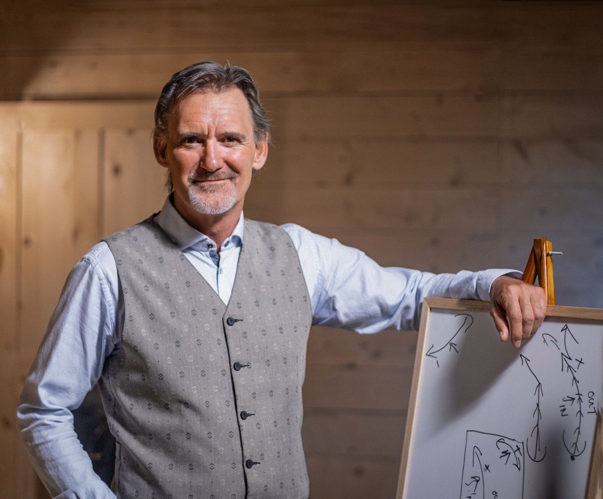 Chris Irwin smiling in a vest with grey bear and his arm resting on a whiteboard