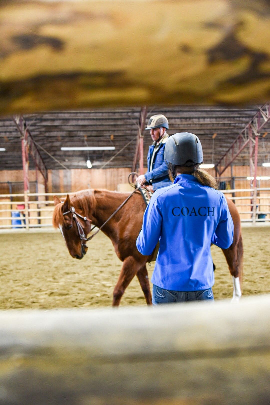 Coach with a blue jacket teaching a male riding western and wearing a helmet